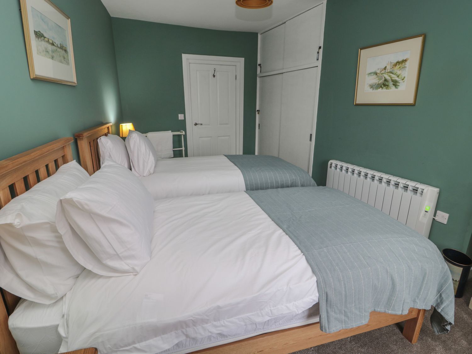 A bedroom with two beds, a white radiator, and a door in the background.