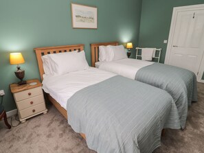 Een slaapkamer met twee bedden, een nachtkastje met een lamp, een lijst met een foto aan de muur, en een witte deur.