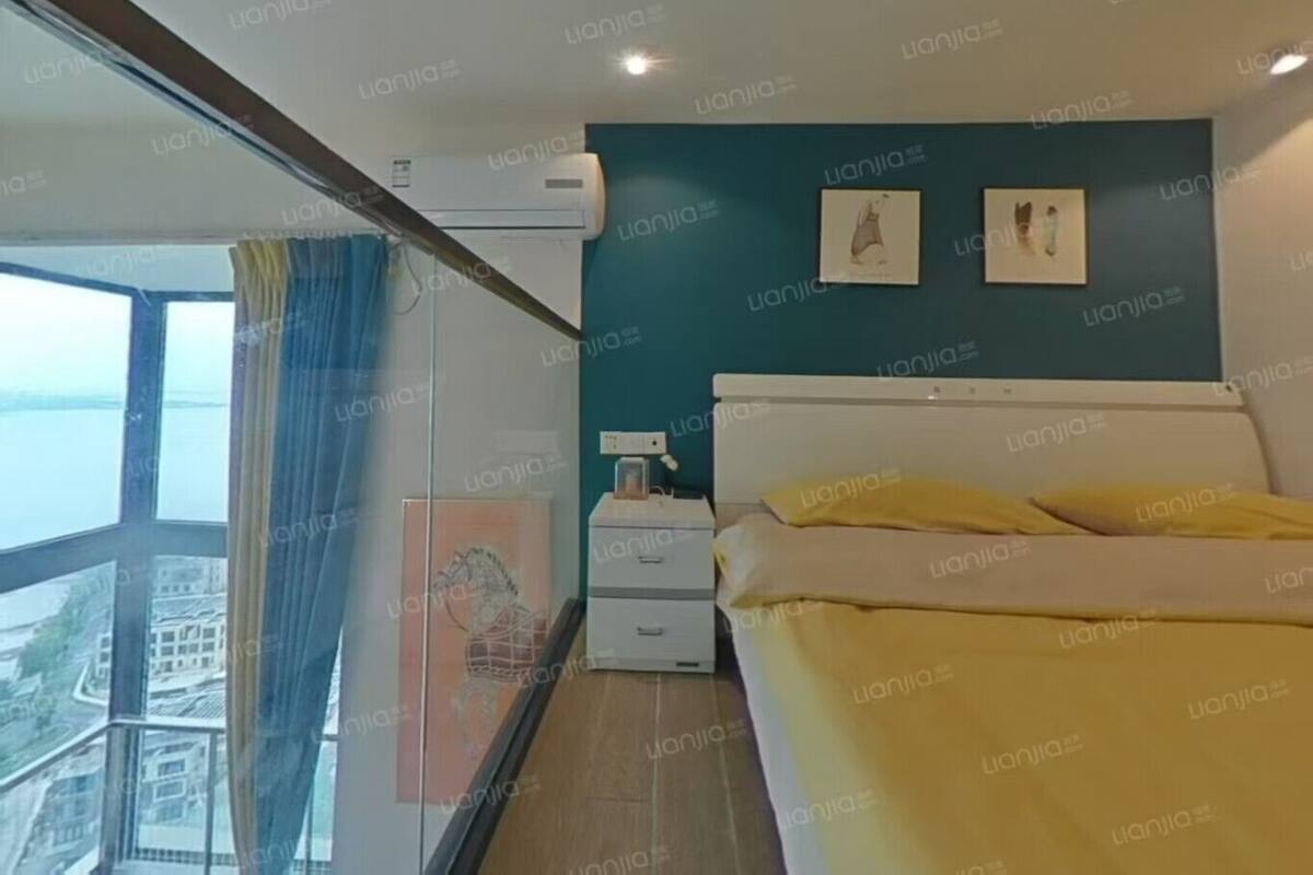 Een slaapkamer met een groot raam, een bed, een nachtkastje en een wandairconditioner.