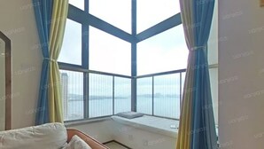 A room with a large window, a bed, and a view of the city.