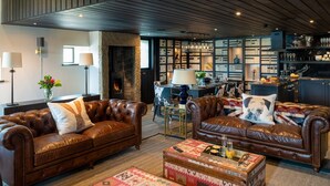 A spacious living area with leather sofas, a fireplace, a bar area, and a bookshelf. - Gunner Lodge (Carnforth)