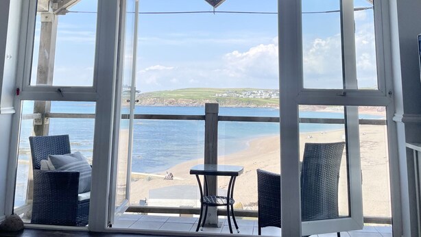A room with a large window overlooking a beach and sea, featuring wicker furniture and a small table. - 12 Thurlestone Rock (Kingsbridge)
