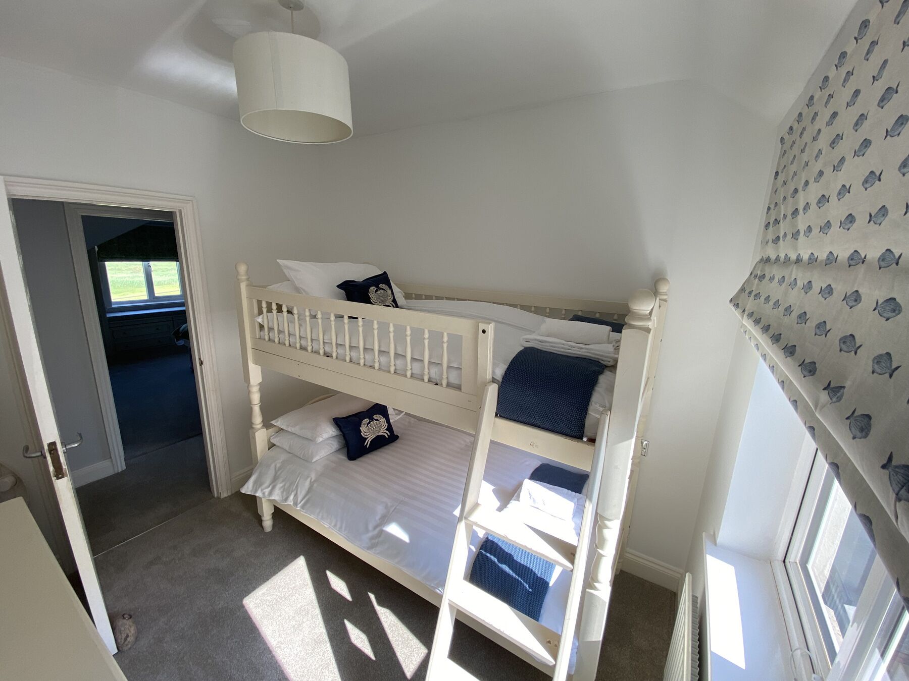 A bunk bed room with a door leading to another room, a window with curtains, and a ceiling light.