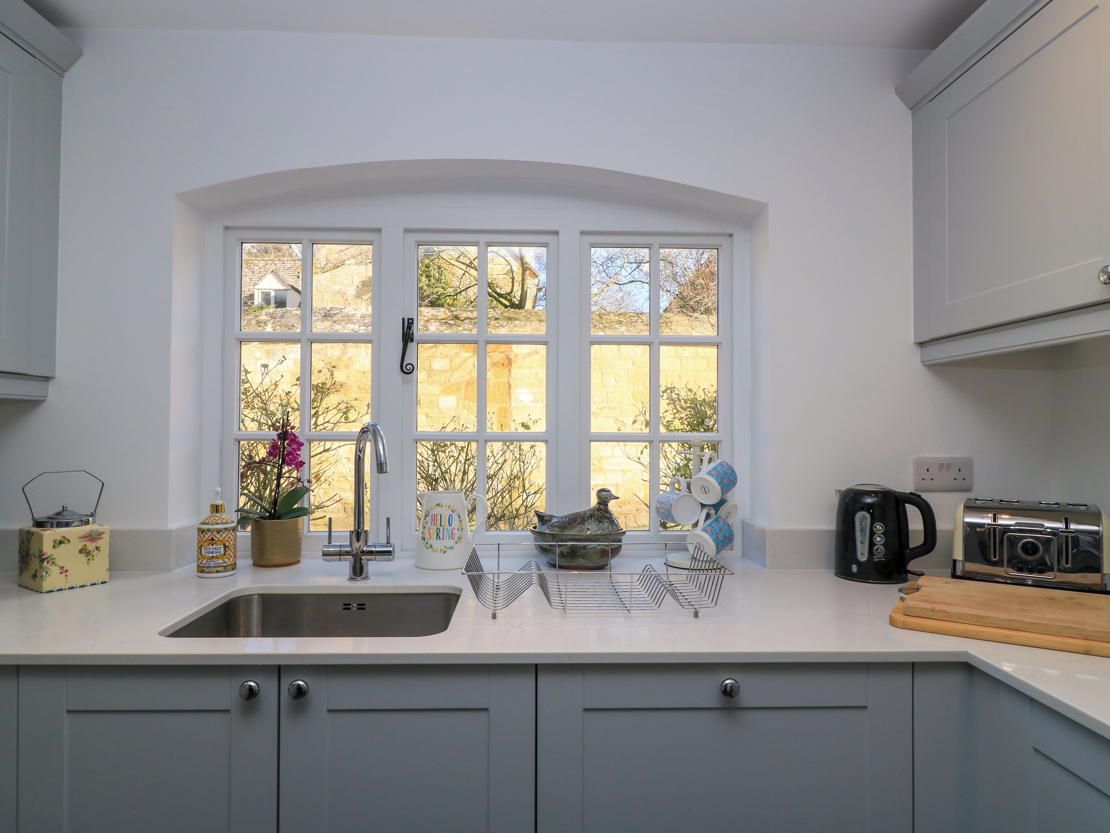A kitchen with a large window, a sink, a kettle, and a toaster.