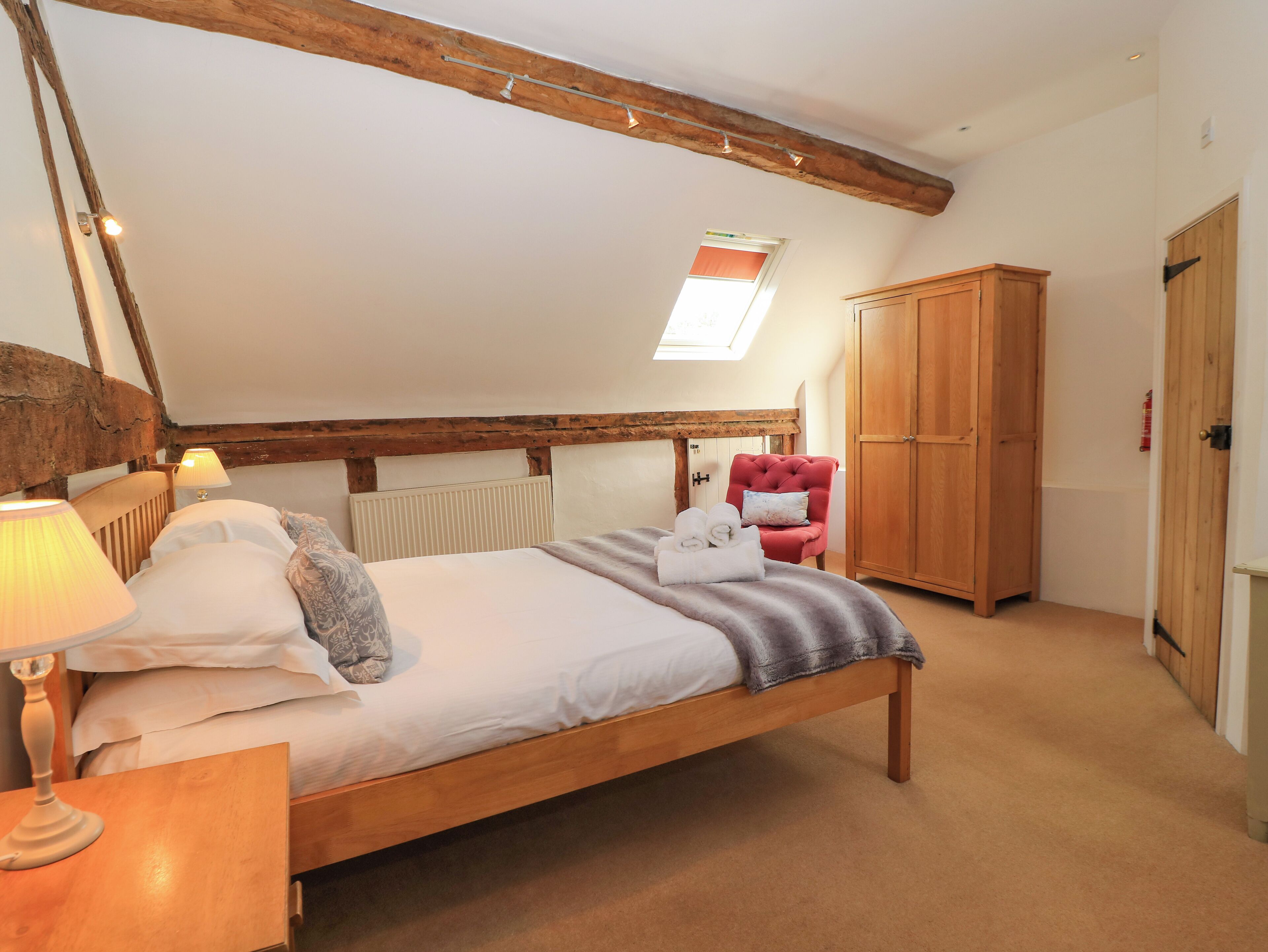A bedroom with a wooden bed, a red armchair, a wardrobe, and a skylight.