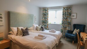 A hotel room with two beds, a chair, a table, and a window with curtains. - 22 Dart Marina (Dartmouth)
