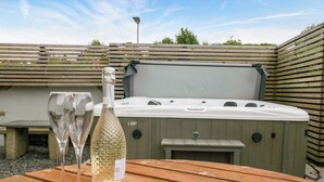A wooden table with a bottle and two glasses, a hot tub, and a wooden fence in the background. - Lund House (Ulverston)
