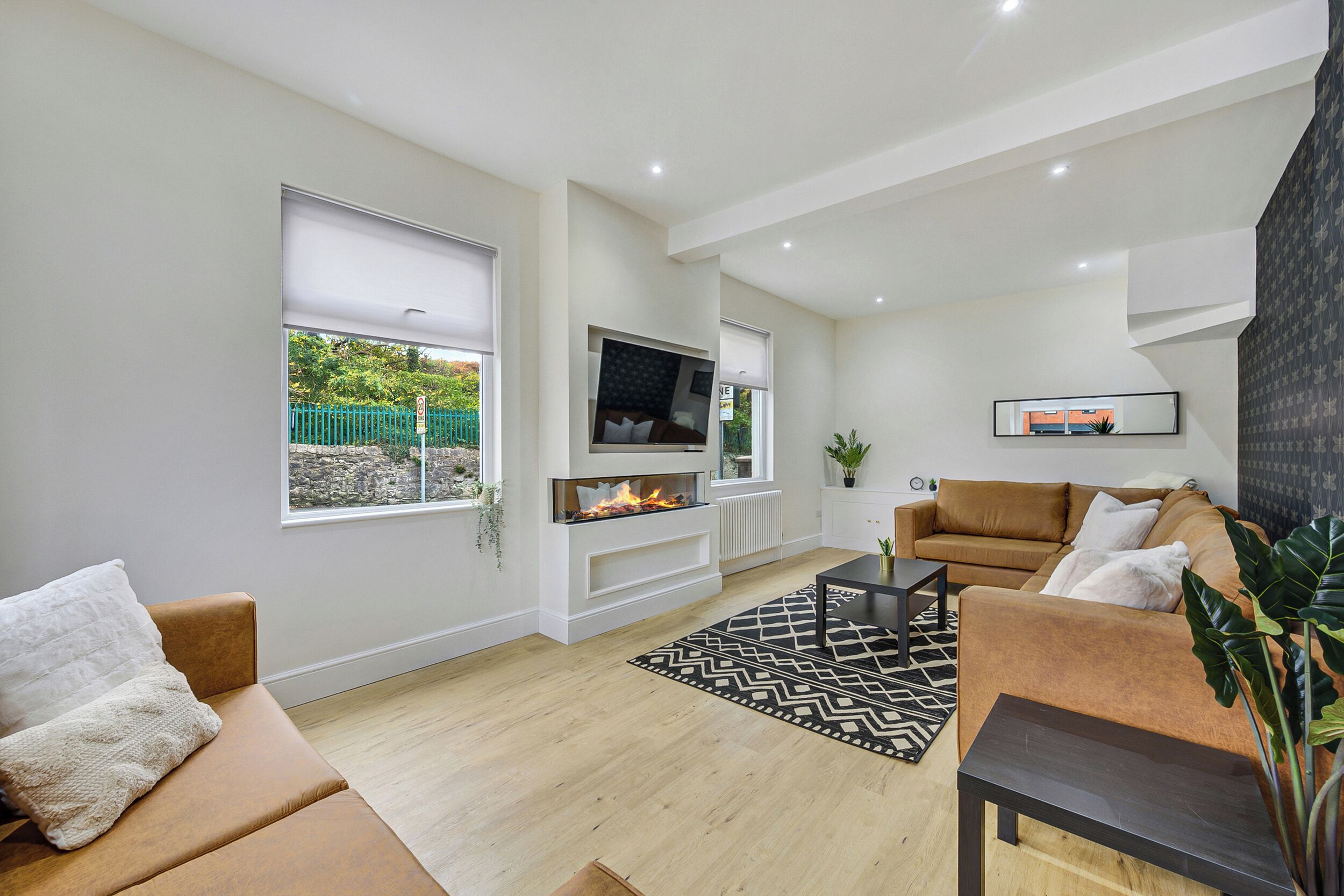 A modern living room with a fireplace, two sofas, a coffee table, and a TV mounted on the wall.