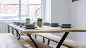 A long wooden table with grey bowls and woven baskets, set against a white wall with a window overlooking a building. - Lund House (Ulverston)