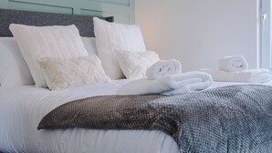A neatly made bed with white linens and a grey knitted throw blanket. - Lund House (Ulverston)