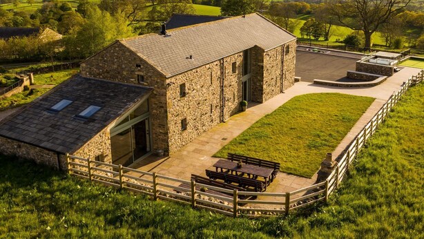 A stone building with a large garage door, a covered outdoor seating area, and a view of rolling hills and wind turbines in the background.