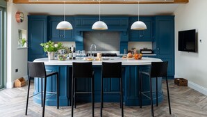 A modern kitchen with blue cabinets, a central island with bar stools, pendant lighting, and a built-in oven.