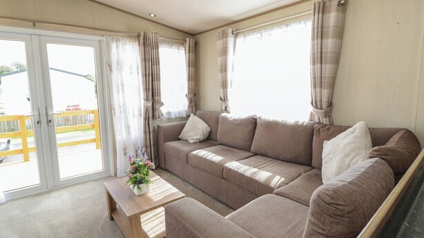 Ein gemütliches Wohnzimmer mit einem braunen Sofa, einem Holztisch und einer Schiebetür zu einem Außenbereich.