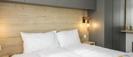 Ein Schlafzimmer mit Holz-Kopfteil, einem Bett mit weißer Bettwäsche, einem Nachttisch und einer Wandleuchte.