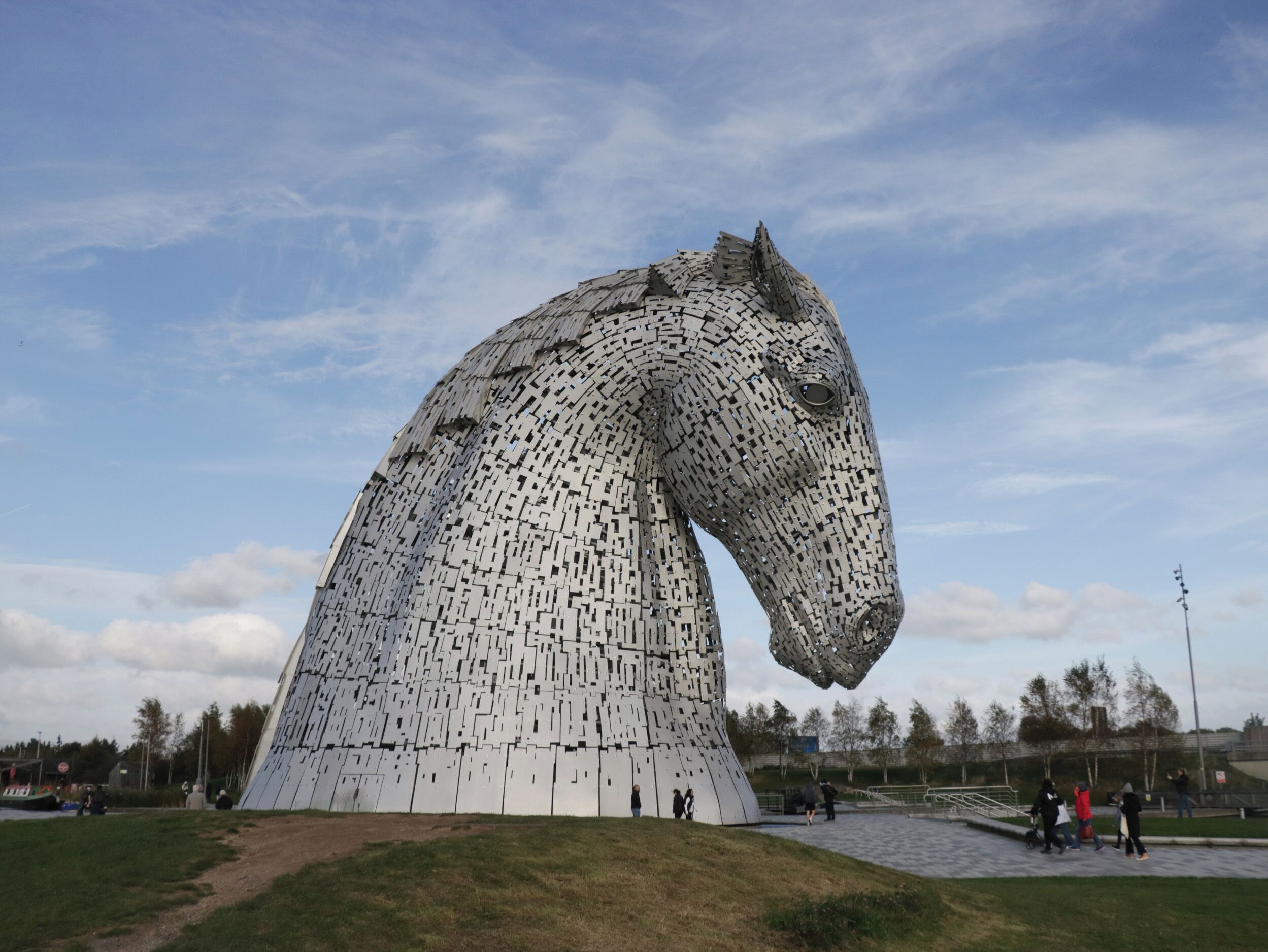 Une grande sculpture métallique représentant la tête d’un cheval, entourée d’une zone herbeuse et d’un chemin pavé.
