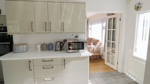 A kitchen with white cabinets, a microwave, and a kettle on the counter. - Howard Cottage (Evesham)
