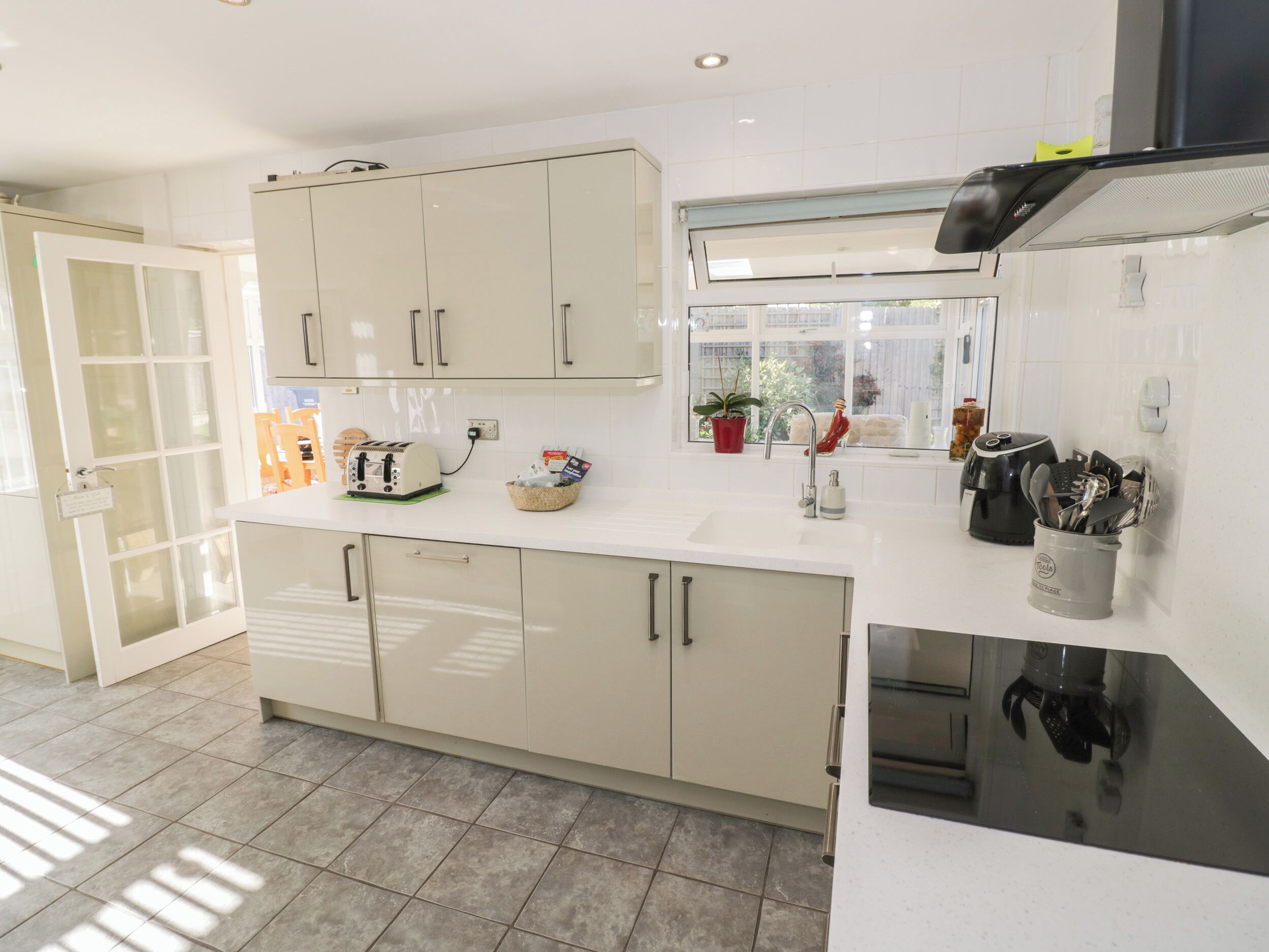 A modern kitchen with white cabinets, a built-in oven, and a window overlooking a garden.