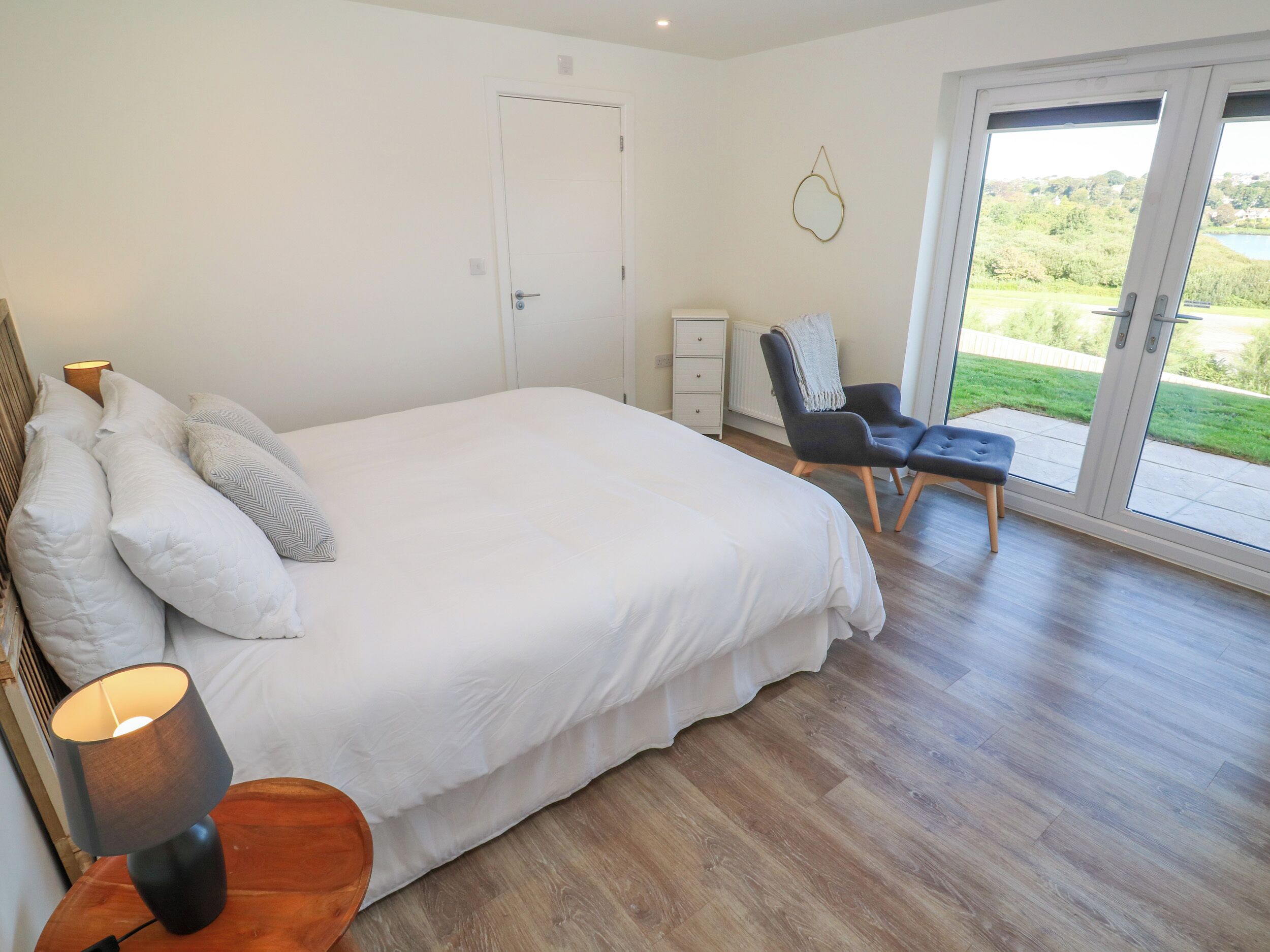 A bedroom with a large bed, a chair, a desk, and a view of the outdoors.