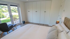 A bedroom with a large bed, a chair, a wardrobe, and a view of the outside. - 2 The Dunes (Falmouth)