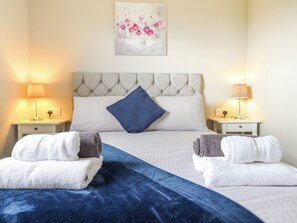 A double bed with a tufted headboard, two bedside tables with lamps, a blue throw blanket, and two folded towels. - Orchard Lodge (Corwen)