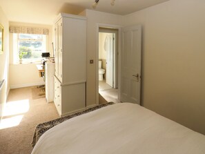 A bedroom with a bed, a wardrobe, a desk with a computer, and a window with curtains. - Valley View Cottage (Holmfirth)