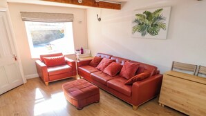 A living room with a red leather sofa, matching ottoman, and a wooden side table. - Valley View Cottage (Holmfirth)