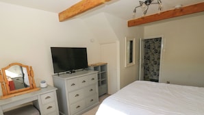 A bedroom with a bed, a TV on a dresser, a wardrobe, and a door with patterned curtains. - Valley View Cottage (Holmfirth)