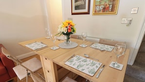 A dining table set with floral placemats, a vase with flowers, and wine glasses. - Valley View Cottage (Holmfirth)