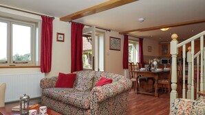 A living room with a patterned sofa, a wooden coffee table, and a dining area with a wooden table and chairs. - Sherway Shippen (Exeter)