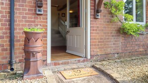 A brick building entrance with a white door, a potted plant, and a welcome mat. - Sherway Shippen (Exeter)
