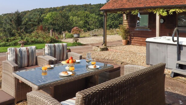 An outdoor dining area with wicker furniture, a glass table, and a hot tub. - Sherway Shippen (Exeter)