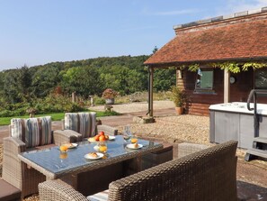 An outdoor dining area with wicker furniture, a glass table, and a hot tub. - Sherway Shippen (Exeter)