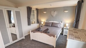 A bedroom with a bed, bedside tables, a wardrobe, a mirror, and a decorative wall piece. - Jacob's Retreat (Skegness)