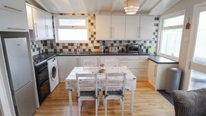 A compact kitchen with a dining table, chairs, a washing machine, a refrigerator, and a microwave. - Jacob's Retreat (Skegness)