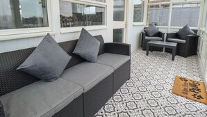 A sunlit patio with a grey sofa, two armchairs, and a small table. - Jacob's Retreat (Skegness)