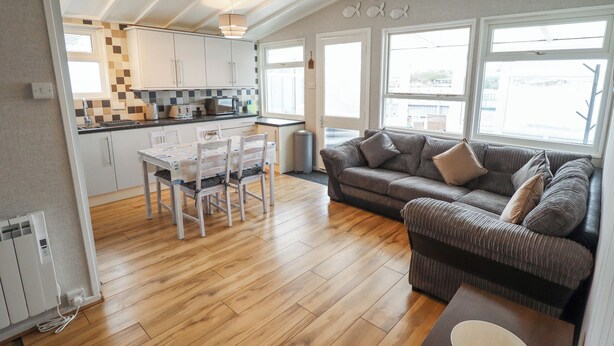A modern kitchen with white cabinets, a dining table with chairs, and a large window. - Jacob's Retreat (Skegness)