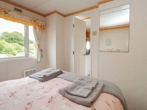 A bedroom with a bed, a window with curtains, a mirror, and a door leading to another room. - Holly (Denny)