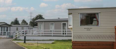 A row of mobile homes with a grassy area in front, a paved path, and a fence.