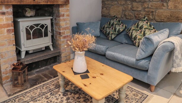 A cozy living room with a stone wall, a blue sofa, a white radiator, and a wooden coffee table with a vase. - The Coquet Nest (Morpeth)