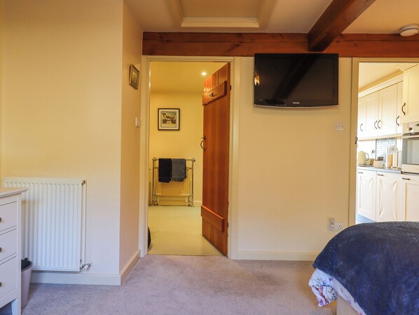 A bedroom with a bed, a TV mounted on the wall, a radiator, and a bathroom visible through an open door.