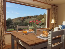 A dining area with a table set for breakfast, a vase with flowers, and a view of a forested landscape.