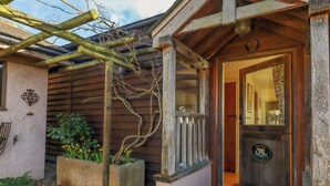 Een rustiek houten huisje met een uitnodigende ingang, een klein terras en een tuin met een pergola en planten.