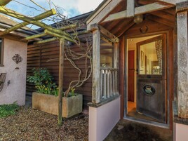 A rustic wooden cottage with a welcoming entrance, a small porch, and a garden area with a trellis and plants.