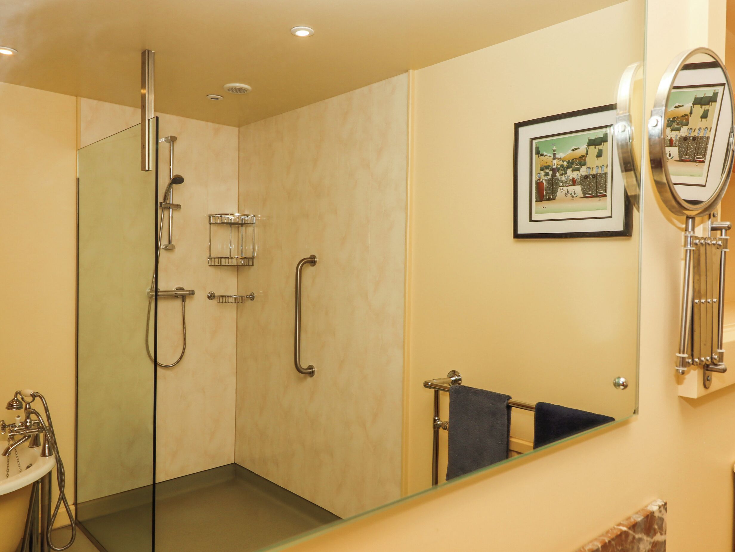 Un bagno con cabina doccia in vetro, lavandino, porta asciugamani e un quadro appeso al muro.