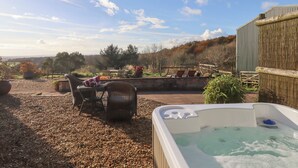 Een hottub in een overdekte buitenruimte met rieten meubels en uitzicht op het landschap.