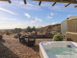A hot tub in a covered outdoor area with wicker furniture and a view of the countryside.