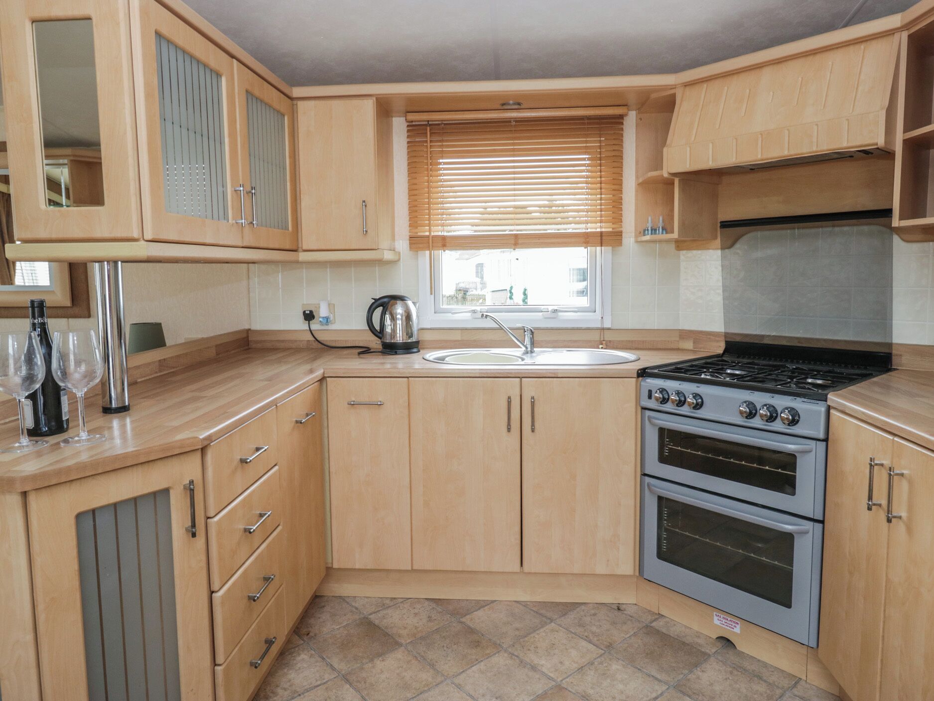 A compact kitchen with wooden cabinets, a gas stove, a sink, and a window with blinds.