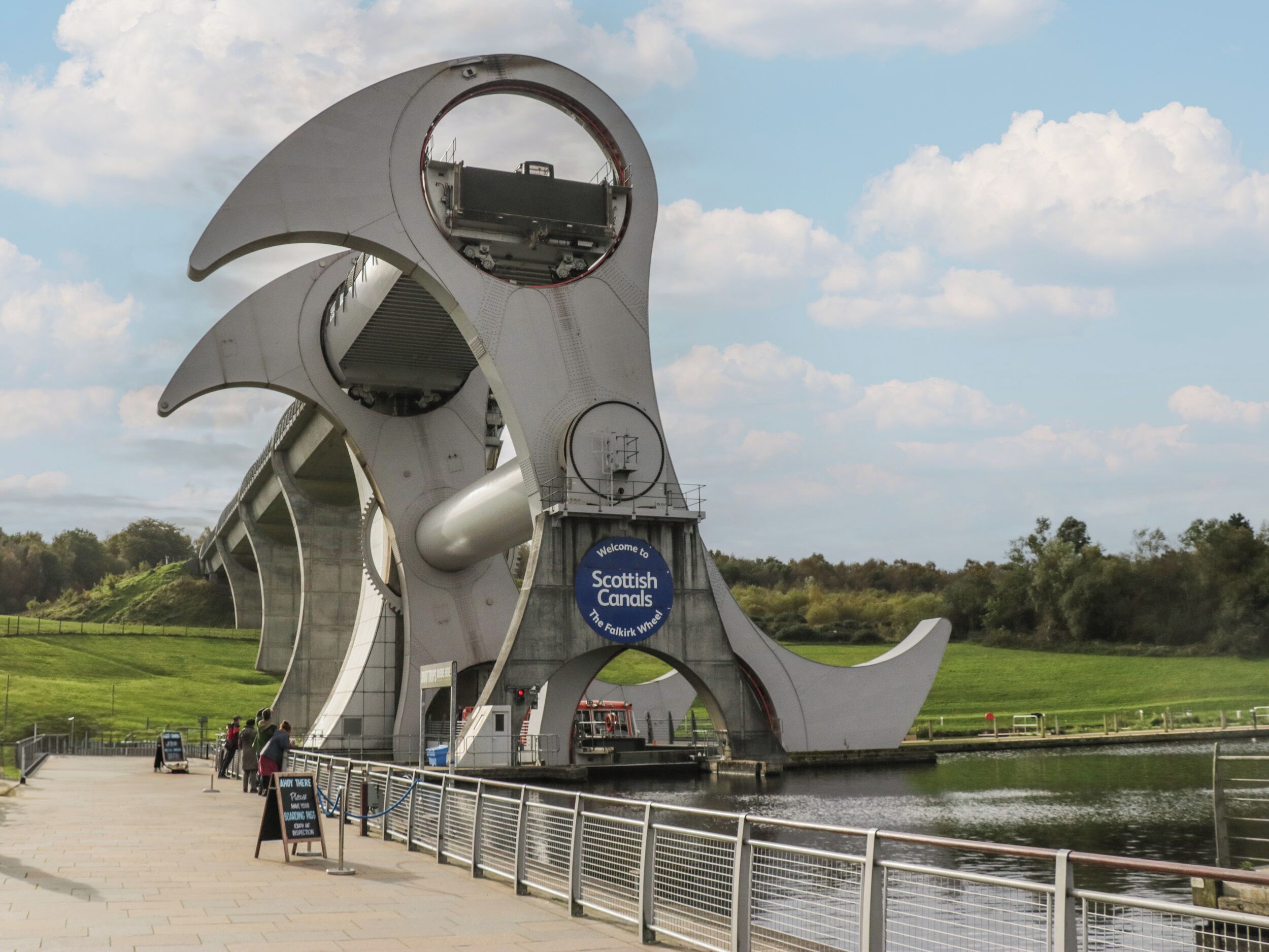 A modern architectural structure with a circular viewing platform and a sign welcoming visitors to Scottish Canals.