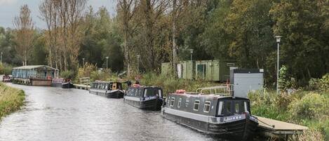Un canal bordé d’arbres et de verdure, où des péniches sont amarrées le long des berges.