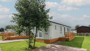 Une maison mobile de plain-pied avec une terrasse en briques, une terrasse en bois et un petit arbre au premier plan.